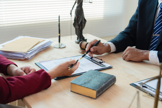 A close-up image of the scales of justice, showing a lawyer holding a law book and reading a contract, with the scales of justice in hand as he advises his client, and the contract documents on the ta