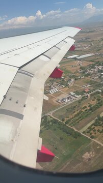 View from Airplane Window: Overlooking a picturesque landscape of fields and buildings from the window of an airplane, with the wing clearly visible in the foreground. Yerevan, Armenia