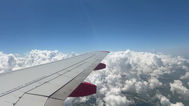 Airplane Wing Above Clouds: A clear blue sky stretches above a sea of fluffy white clouds, with the wing of an airplane piercing through the atmosphere, offering a breathtaking view from the sky.
