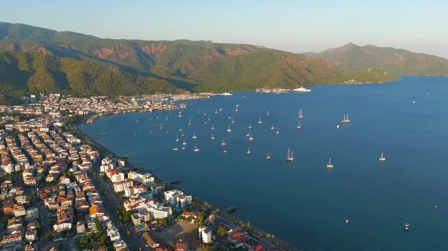 Marmaris, Turkey. Aerial view of the natural harbour at golden hour, sailboats on calm water and terracotta rooftops against pine-covered mountains. Aerial View