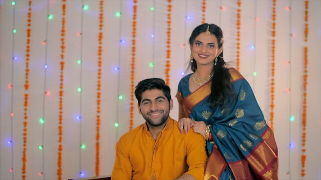 Handsome Indian husband happy to see his wife in traditional saree on Diwali. Medium shot of a newly married couple in traditional clothes in their living room during a Hindu festival celebration