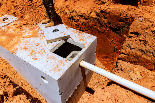 Workers install concrete septic tank into trench at construction site ground is dry with some dirt, rocks.