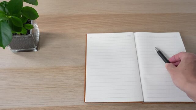 Hand placing a pen on an open notebook at a minimalist workspace
