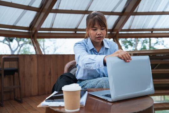 Woman in blue shirt is engaged in financial planning and data analysis while working on laptop in wooden room with coffee cup and documents on table during discussion