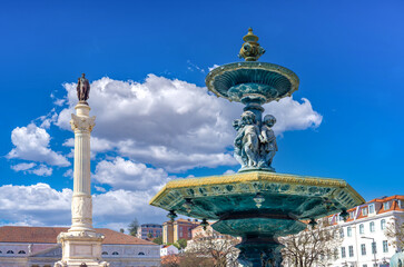 Obraz premium An ornate bronze baroque fountain near the monumental Column of Pedro IV under a vibrant blue sky with clouds at the historic Rossio Square in Lisbon Portuga