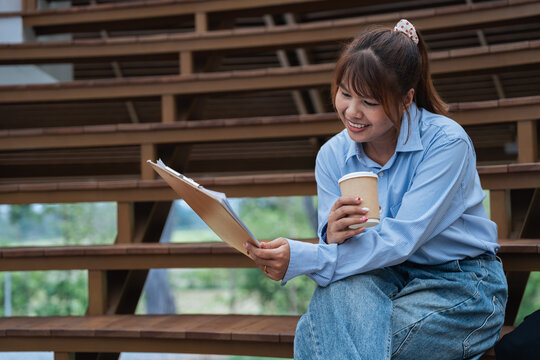 Young woman enjoys coffee while reviewing data and financial documents during planning discussion outdoors, showing focus and positive engagement in analysis work