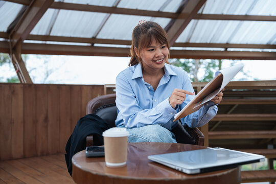 Young woman smiling while holding paper document during financial planning discussion with data and analysis on table in cozy wooden office