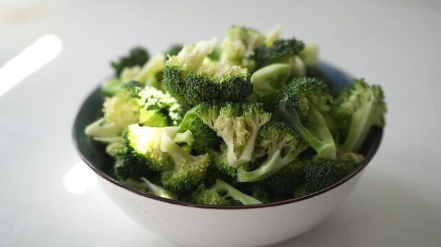 Fresh broccoli florets cut into bite-sized pieces and served in a bowl on a white surface, ready for cooking or healthy meals. Broccoli is rich in vitamins, minerals, and dietary fiber