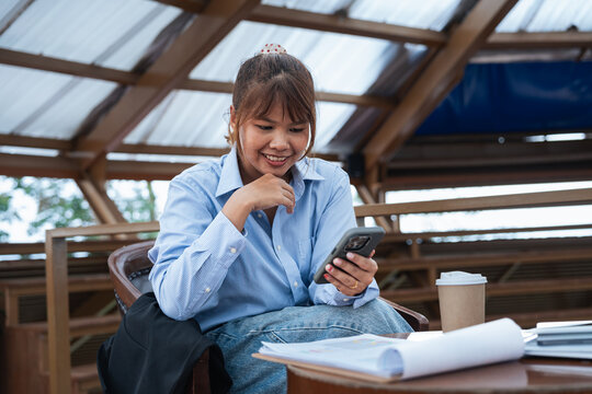Young woman using smartphone for data analysis and financial planning while having discussion in casual workspace with documents and coffee cup on table