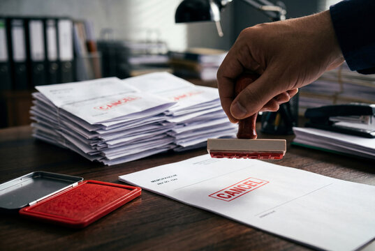 Hand using red cancel stamp on documents at office desk