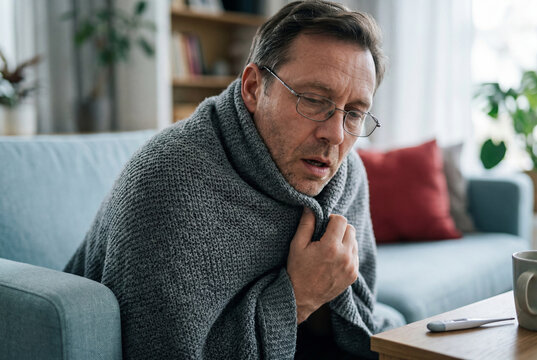 Sick man wrapped in blanket experiencing fever symptoms at home