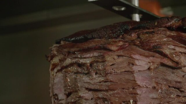 Close Up of Sirloin Meat Being Carved from Trompo onto Tortilla. Taquero Carving Sirloin Meat from Vertical Spit. Traditional Sirloin Taco Preparation on Trompo. Close Up of Beef Sirloin.