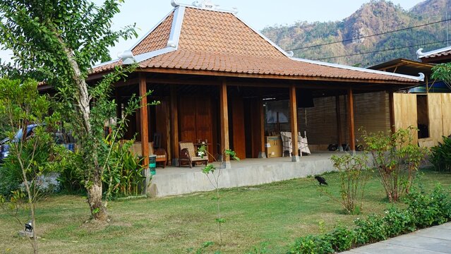 Traditional Javanese Joglo House with Wooden Pillars and Clay Tile Roof against Scenic Hill Background