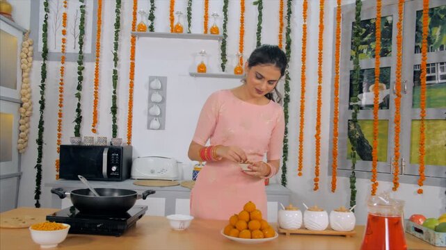 Beautiful Indian woman decorating the bowl of laddus in the kitchen . Medium shot of a lovely Indian married couple feeding each other happily - Indian festival