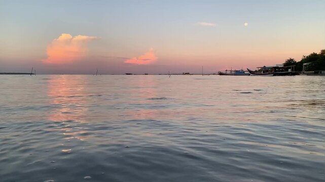 4K coastal sunset footage at Tanjung Lesung Beach, Banten, Indonesia. Gentle waves ripple along the shoreline with soft natural ocean sounds, calm water reflections, pastel clouds, and a peaceful trop