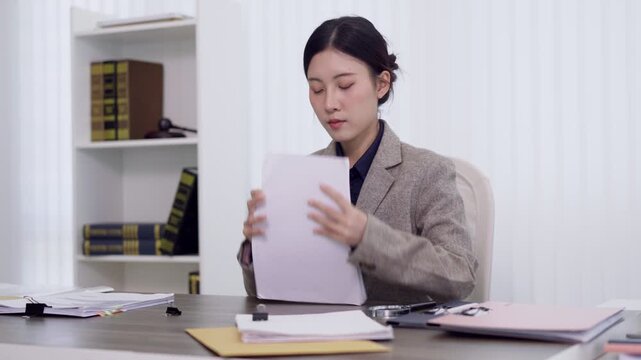 Asian female lawyer professional review legal document contract paperwork at modern law office desk workplace studying case file litigation preparation