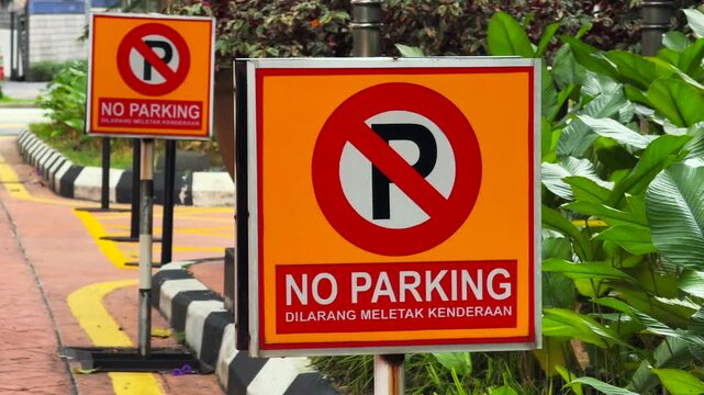 Close up of Bilingual No Parking Signs in English and Malay on City Street near black and white striped bardur 