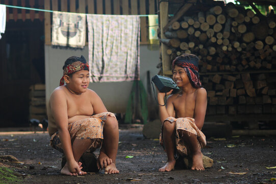 Two Asian boys from rural Indonesia happily listening to a vintage transistor radio in their traditional village