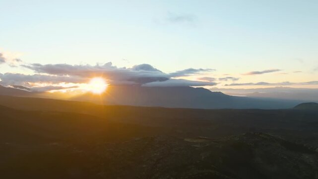 Aerial footage of dramatic sunset light over Tolbachinsky Dol volcanic plateau with clouds and distant mountain silhouettes, Kamchatka Krai, Russia