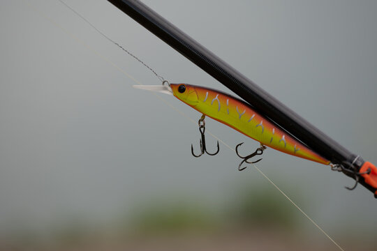 Fishing lure hangs from fishing rod near water in the early morning light