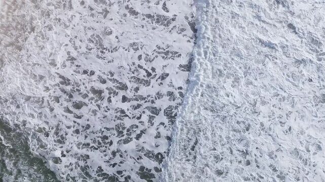 Overhead drone footage of churning ocean surf and white sea foam patterns on dark water, natural marine background texture with copy space for design use