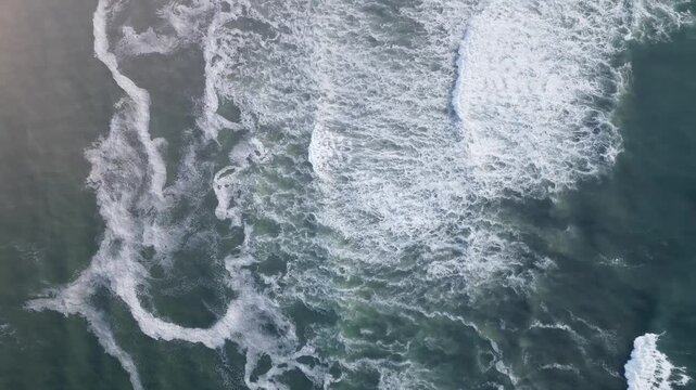 Drone footage looking straight down at rolling ocean waves creating white sea foam patterns on deep turquoise water, natural seascape background with copy space