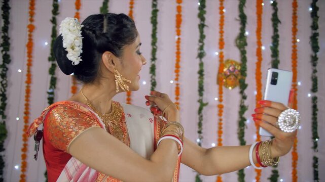 Side view shot of a beautiful female happily talking to her friends on a video call. Smiling Bengali woman showing her traditional outfit and Durga Puja festival decorations on a group video chat