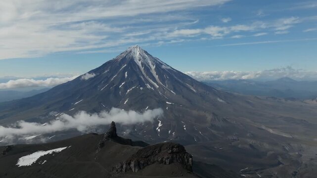 Drone footage of Koryaksky volcano with snow patches on the cone and low clouds drifting over volcanic slopes, Kamchatka Krai, Russia, on a clear day