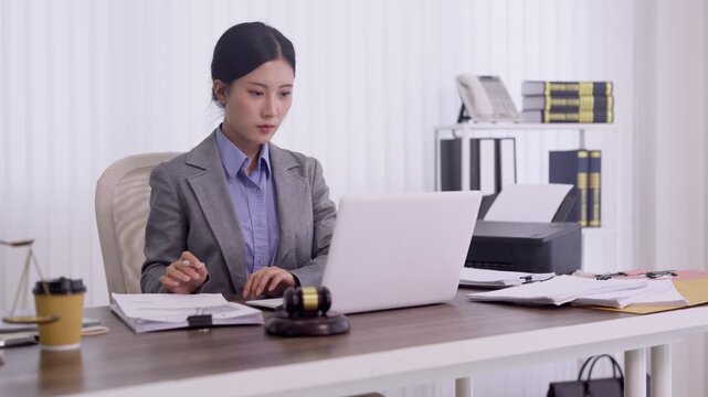 Asian female lawyer reviewing legal documents using laptop computer with gavel on desk in modern law office professional attorney preparing case research