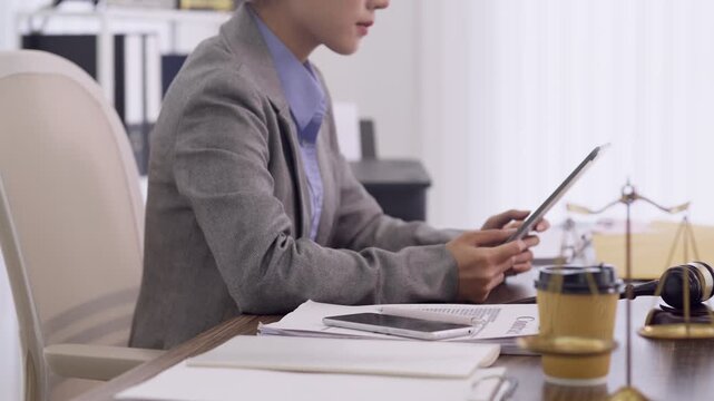 Asian lawyer businesswoman use tablet device review legal document case file research law firm office desk with scale justice gavel symbol professional