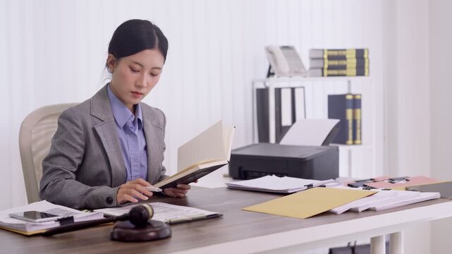 Asian lawyer professional reading legal documents book at office desk with gavel preparing case research studying law reference materials for courtroom trial