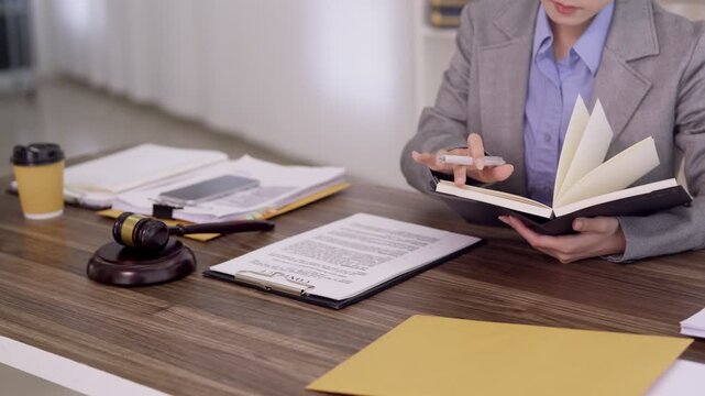 Asian lawyer reading law book reviewing legal documents case files research at office desk with gavel professional attorney studying legislation preparing