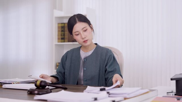 Asian female lawyer reviewing legal documents at office desk with gavel preparing case files for court trial professional attorney working with paperwork in