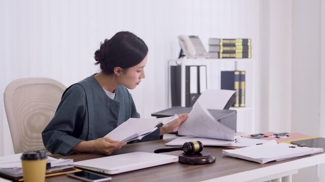 Asian women lawyer review legal document contract agreement paper sitting desk office workspace professional attorney prepare case file work modern law firm