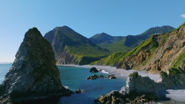 Wide coastal landscape footage of Avacha Bay with rocky beach, turquoise sea and green mountains under clear sky, filmed in Kamchatka Krai, Russia