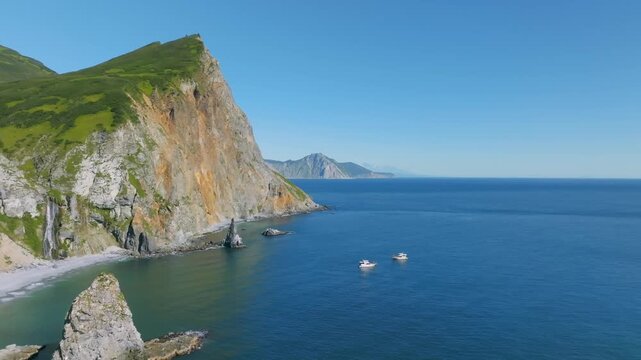 Drone footage of rugged sea cliffs and green slopes above a quiet bay with small boats on calm water in Avacha Bay, Kamchatka Krai, Russia