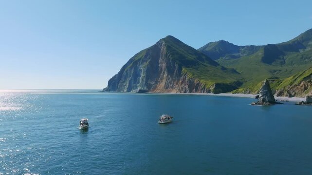 Aerial view of two tourist boats on calm blue water with sun glitter and coastal cliffs in Avacha Bay, Kamchatka Krai, Russia, summer travel seascape