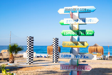 Colorful direction signpost on sandy beach near the sea. Seaside landmark showing distances to world cities. Travel destination concept. Close-up. © Ekaterina