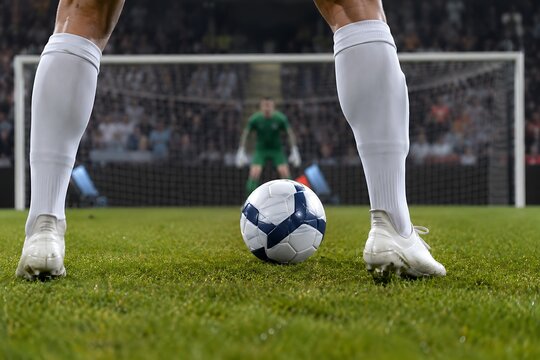 Low-angle close-up from behind the shooter&rsquo;s legs moments before taking a penalty kick