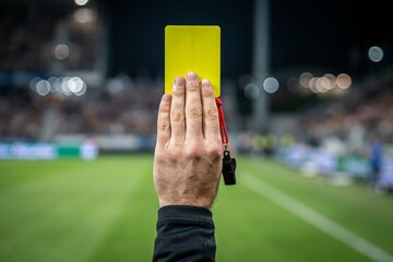 a referee raising a yellow card during a soccer match, whistle hanging between fingers © STUDIO