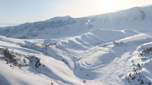 Drone footage of snowy Chunkurchak Valley with ski slopes, winding roads and mountain ridges in winter sunlight, Kyrgyzstan, Central Asia travel scenery