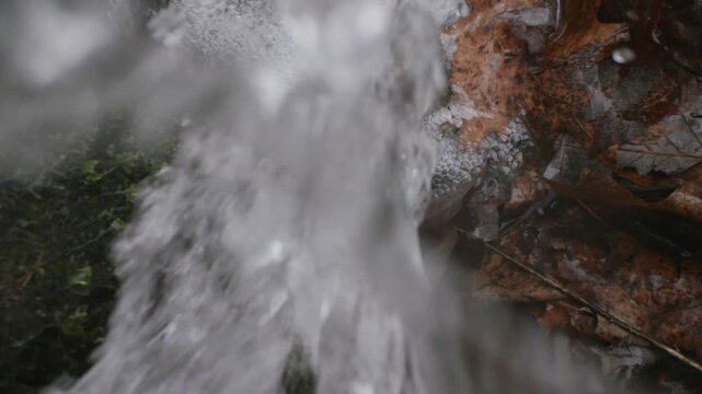 Natural water splash over autumn leaves, fresh mountain stream flowing on forest floor, cinematic slow motion water droplets and brown foliage