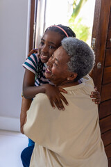 Naklejka premium African American senior woman and child hugging, sharing warm embrace in doorway with wooden door