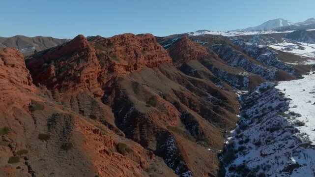 Drone footage of the Jety Oguz Gorge and the Seven Bulls rock formation, red sandstone cliffs and mountain ridges with patches of snow, Issyk Kul Region, Kyrgyzstan