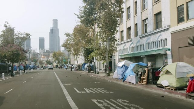 Slow motion drive through Skid Row street lined with homeless encampment tents in downtown Los Angeles.