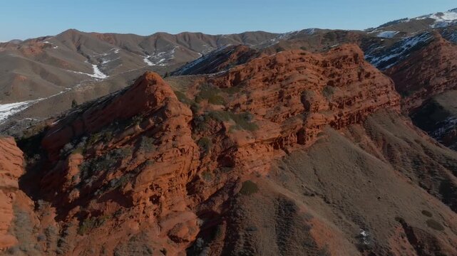 Drone footage of the Jeti Oguz gorge and the Seven Bulls red sandstone cliffs in Issyk Kul Region, Kyrgyzstan, with snowy mountain ridges under clear blue sky