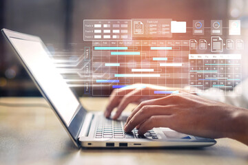 A close-up view of hands typing on a modern laptop, surrounded by a digital project management...