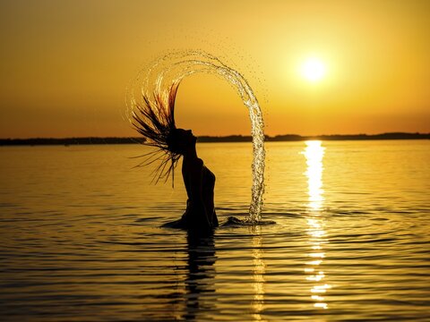 Young woman in the water throws back her long hair with a surge of water, sunset, Chiemsee, Chiemgau, Upper Bavaria, Bavaria, Germany