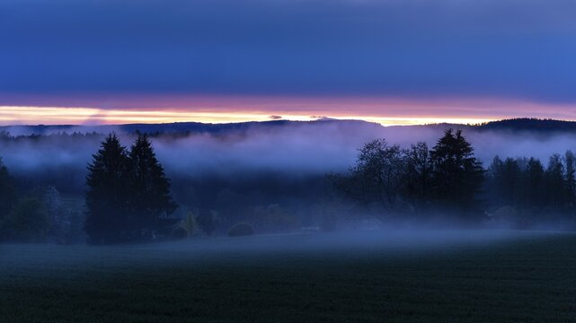 Landscape in the Little Odenwald. Meadow, trees and forest. After sunset, with rising mist (ground fog) and a layer of clouds. Coloured clouds on the horizon. Small Odenwald, Rhine-Neckar district, Baden-W&uuml;rttemberg, Germany