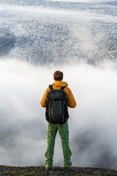 Young man in front of impressive landscape at sunset, fog, clouds moving around, glacier ice of the glacier tongue K&ouml;tluj&ouml;kull, glacier Myrdalsj&ouml;kull, Pakgil, Iceland